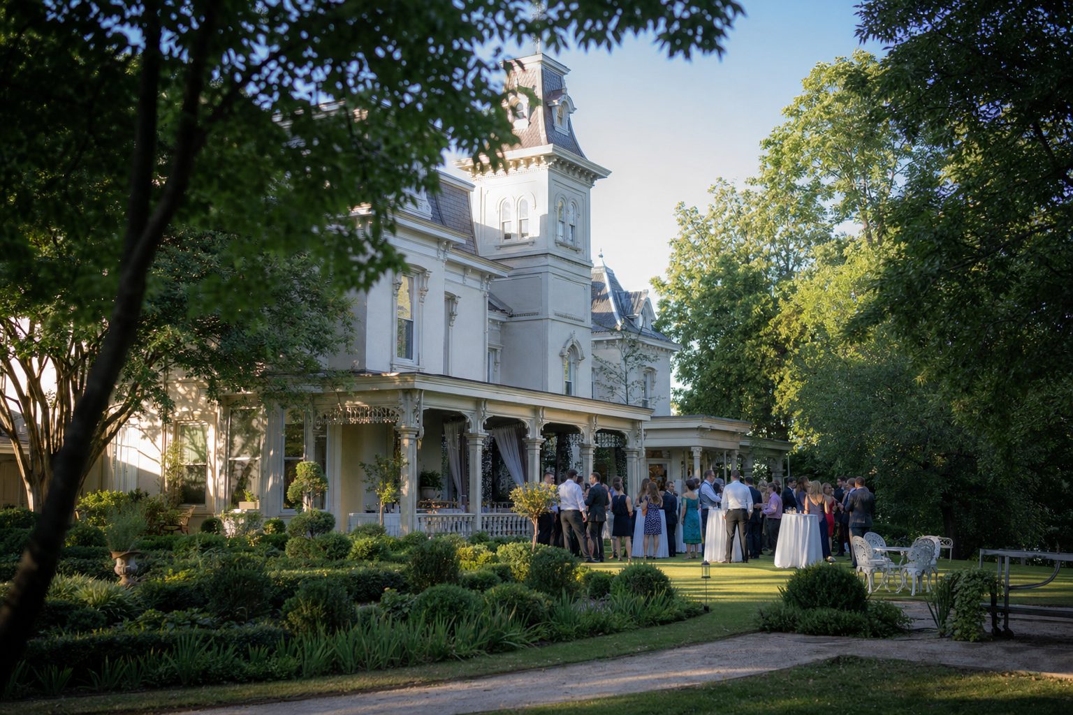 A grand white Victorian mansion with a corner tower and columned porch, guests gathered on the lawn at golden hour, typical of a country-house hotel